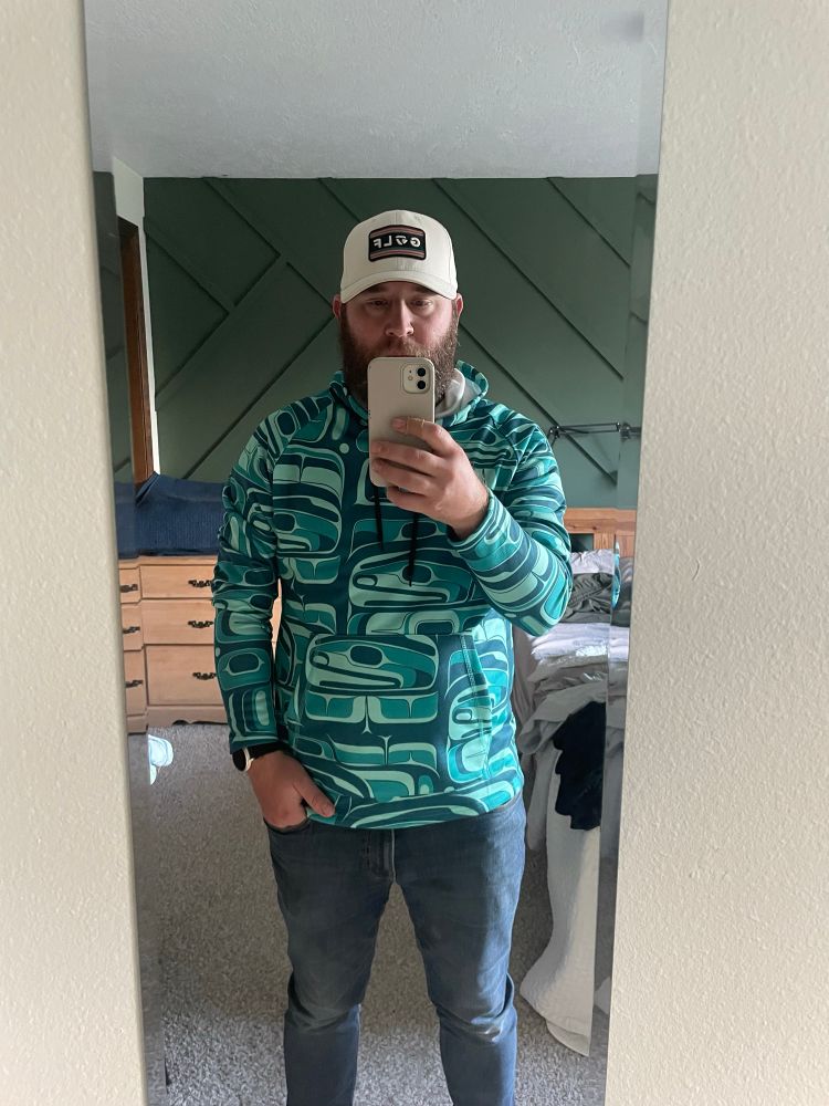 A blue and green hoodie made entirely of drawings of orcas in the style of the First Peoples of the Pacific Northwest