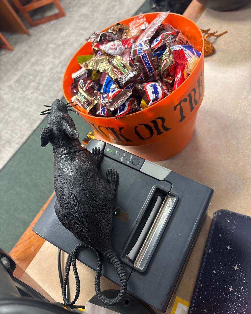 A bucket of candy for trick or treaters sits on a counter. Next to it is a receipt printer with a plastic rat on top 