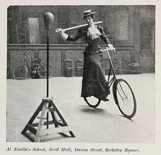 Black and white photo of a woman on a late 19th century bicycle with a saber and a training target
