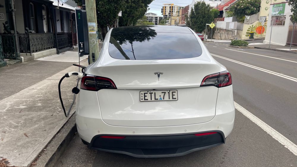 Rear view of a Tesla car charging at a street pole EV charger parked by side of road 