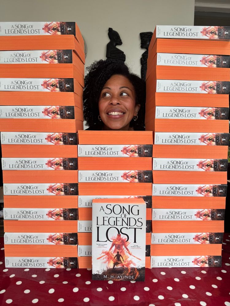 Modupe’s grinning face framed by a stack of paperback copies of A SONG OF LEGENDS LOST