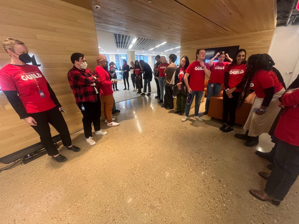 A few dozen people line an office hallway wearing red "GUILD" shirts.