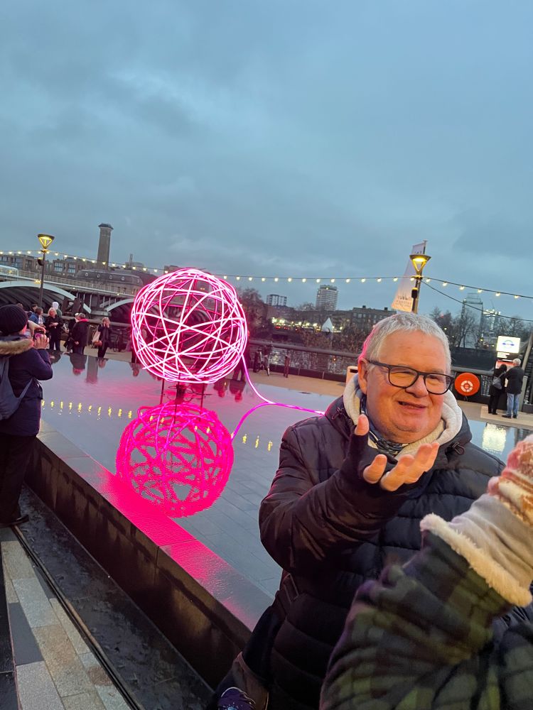 iPhone photo of our host in front of a pink ball of light installation on a water feature 