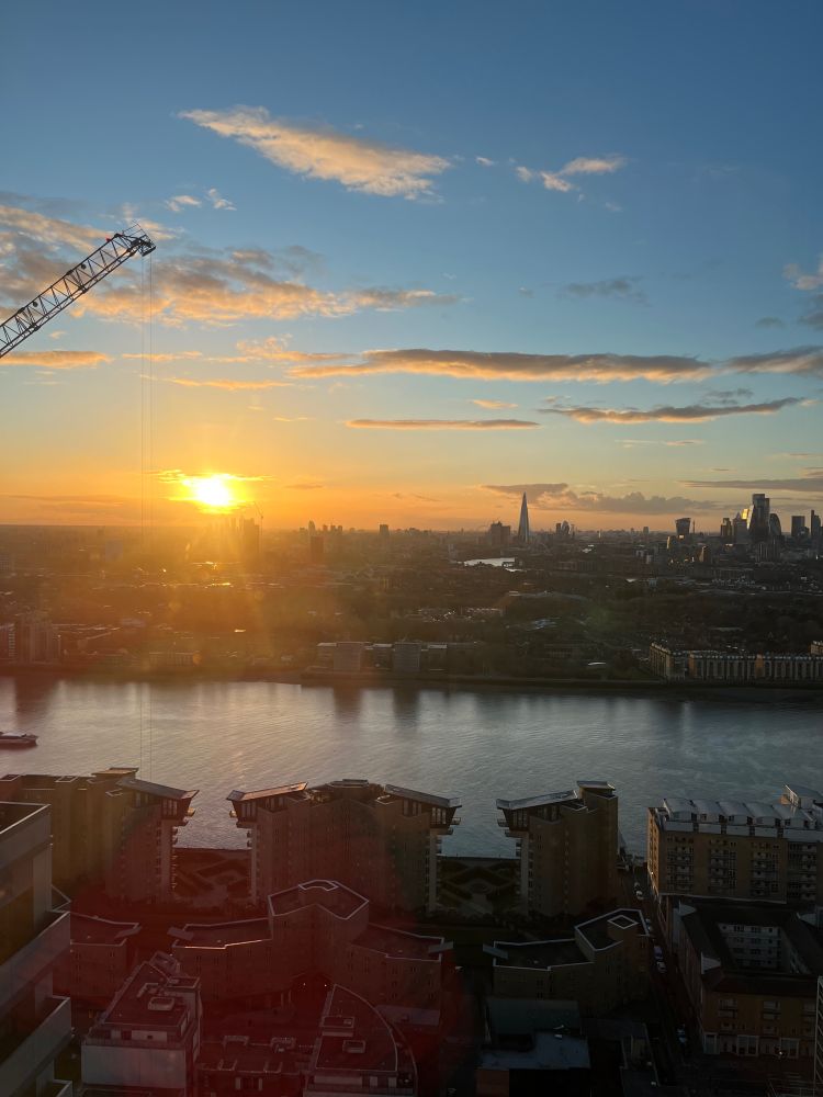 iPhone photo from Bokan bar, 38th floor of Novotel showing view west across the Thames and wide vista of central London with iconic buildings and skyline, with sun almost set. Canary Wharf golden hour sunset light. 