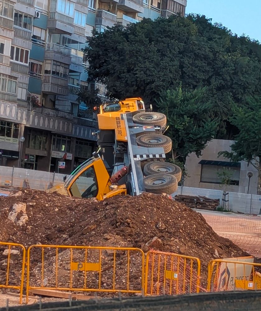 A huge excavator truck on its side. The arm and bucket are inside the hole it was digging, I think.