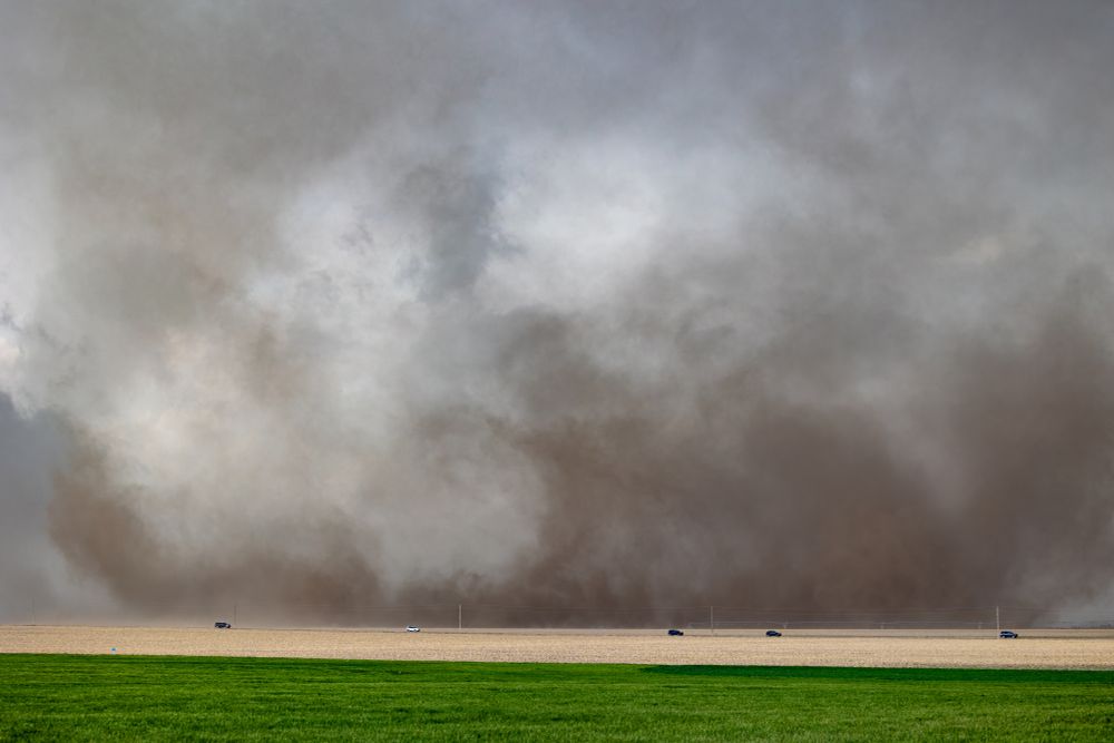 Large tornado forming over the fields of Colorado. Multiple chaser vehicles visible in the foreground.