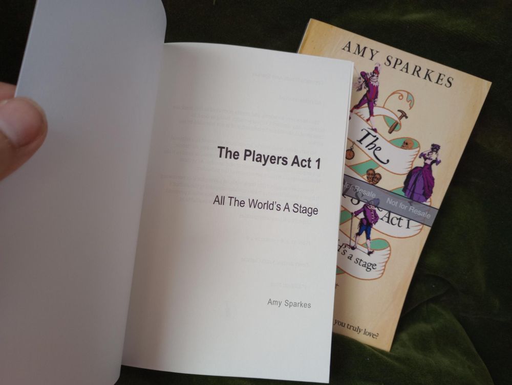 One proof copy is closed and rests on a green curtain. The second copy is opened showing the title page, THE PLAYERS ACT 1: ALL THE WORLD'S A STAGE, Amy Sparkes. 