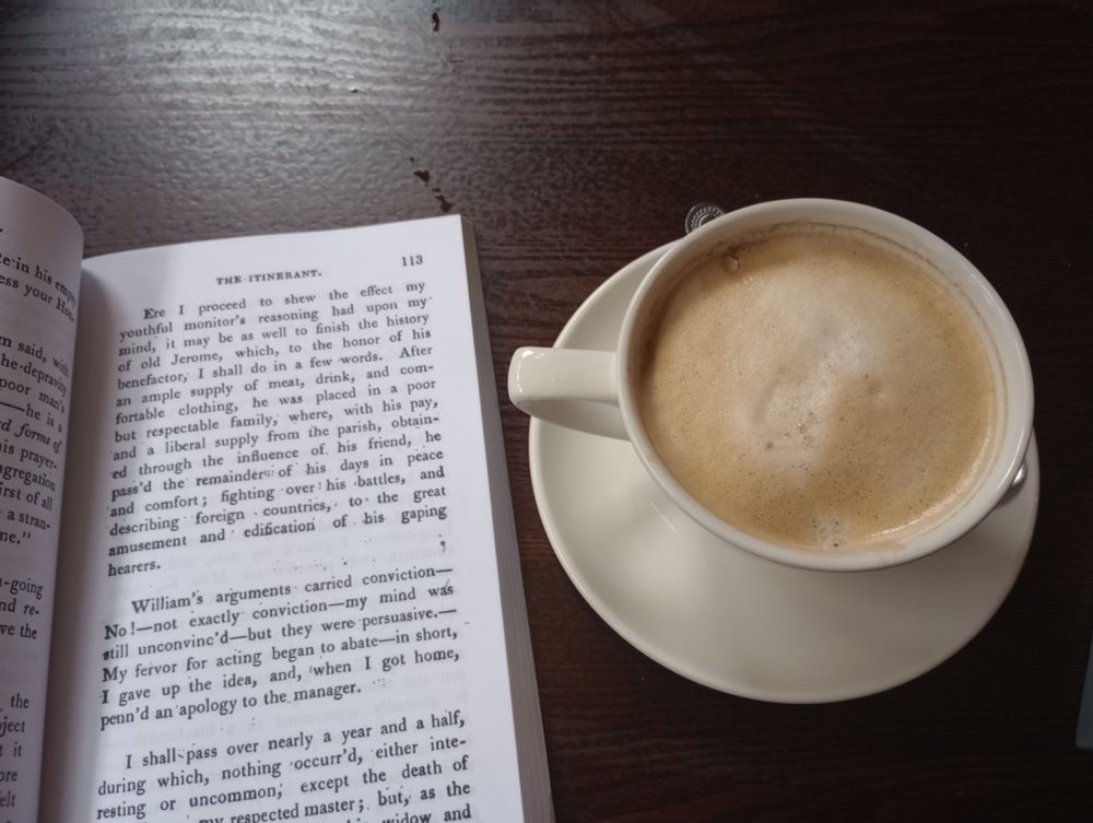 An open copy of 'The Itinerant, Or The Memoirs Of An Actor' by Samuel Ryley on a table, beside a nice cup of coffee. 