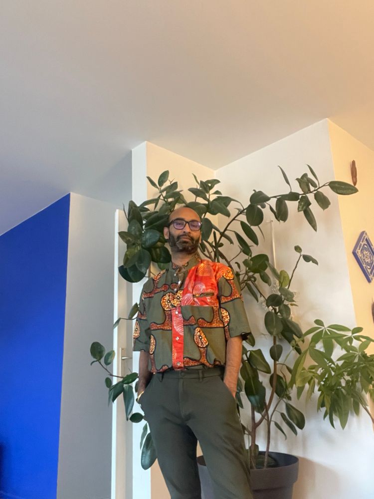 Me in front of a rubber tree in green trousers and red and green wax print shirt 