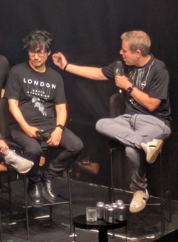 Geoff Keighley reaches out to caress Hideo Kojima’s face. Hideo Kojima looks away, rejecting Keighley’s advances.