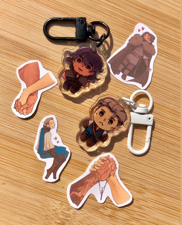 two keychains depicting chibi versions of op's characters Avel and Auden, surrounded by four sticker designs of the same characters. The boys!!!