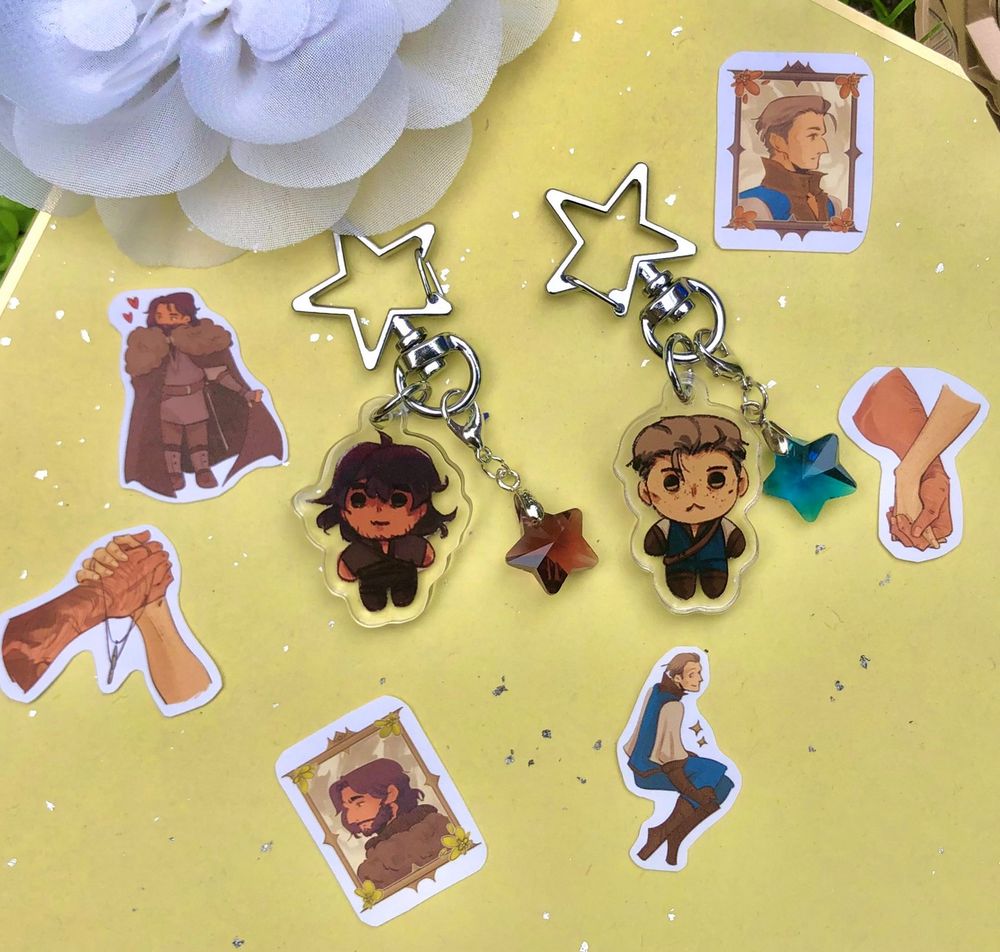 real-life picture showing previews of two keychains, each depicting op's characters Avel and Auden, surrounded by six tiny hand-cut stickers. This picture is a preview of all the items available in op's online shop.