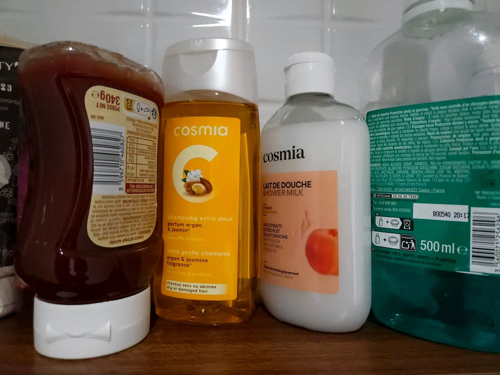 Photo des produits Cosmia dans ma salle de bain. A gauche l’ancienne charte avec un gros C sur fond coloré. A droitela nouvelle charte plus sobre avec une typo serif. Tout a gauche. Un flacon de ketchup 