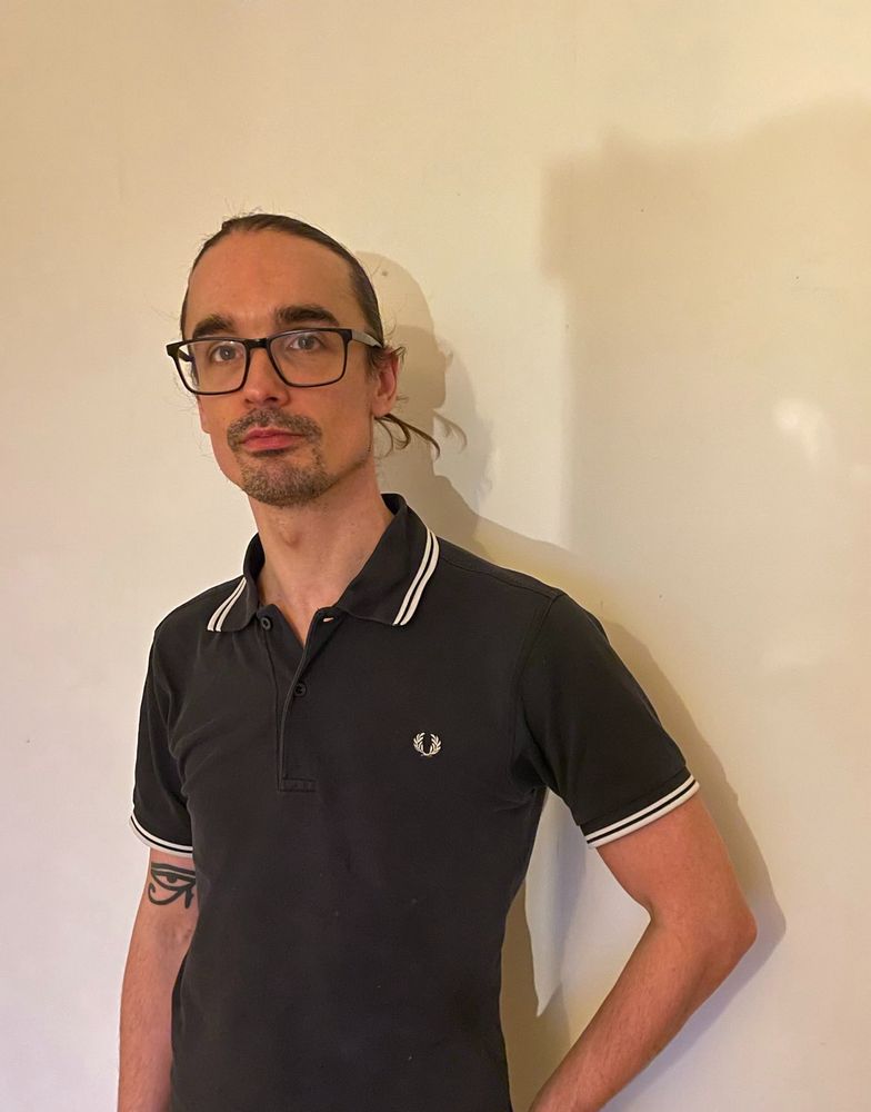 Björn pictured wearing a black polo neck shirt, black-rimmed glasses, and a tattoo on his right arm.