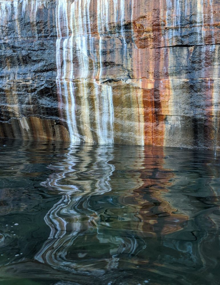 I took this photo while kayaking on Lake Superior. The cliffs of Pictured Rocks National Lakeshore had a lot of interesting sights and this was one of my favorite captures. Minerals seeping out of the rocks create multicolored abstract lines that run into the lake, and then ripples from the water reflect the lines as if they are spilling onto the surface and become fluid. The colors are bright white, Rusty red, sulfur yellow, black, and a variety of browns.