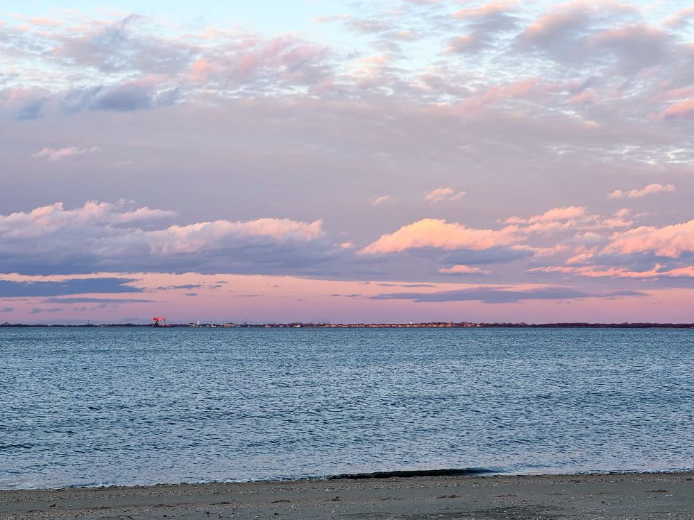 Photo of a view across the Sandy Hook Bay, with a pink and blue sky.