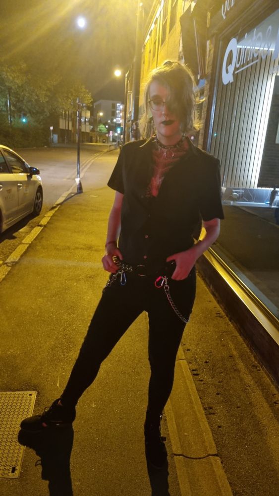 Pic of me last night. Orange af street lights. Wearing a button up shirt with the sleeves cut off. Buttoned up a bit but enough buttons undone to show off the body glitter art I did which looks like a ribcage. Hair half up with the rest framing my face. Several studded and spiked belts, chains and carabiners. Heels and skinny jeans. Black lipstick. Leaning on one leg with my hands on my belt.