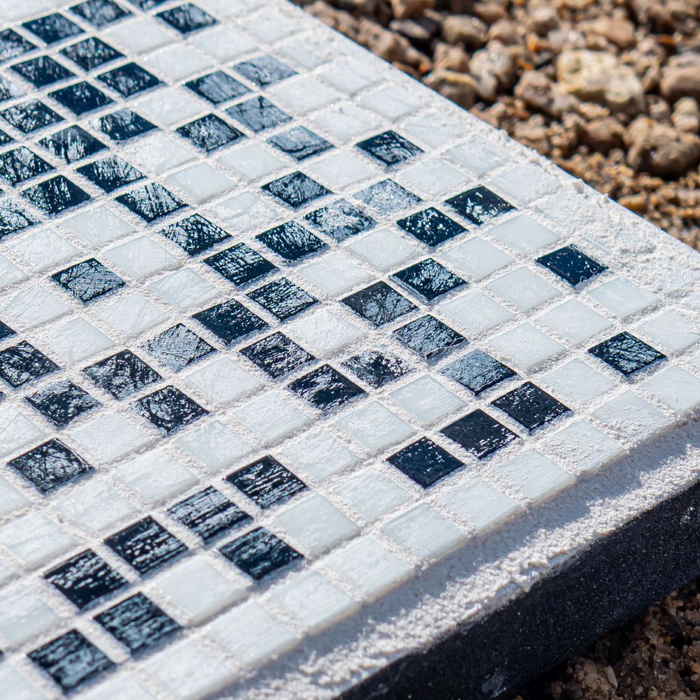Detail photo of poorly cleaned grout on top of black and white glass tiles.