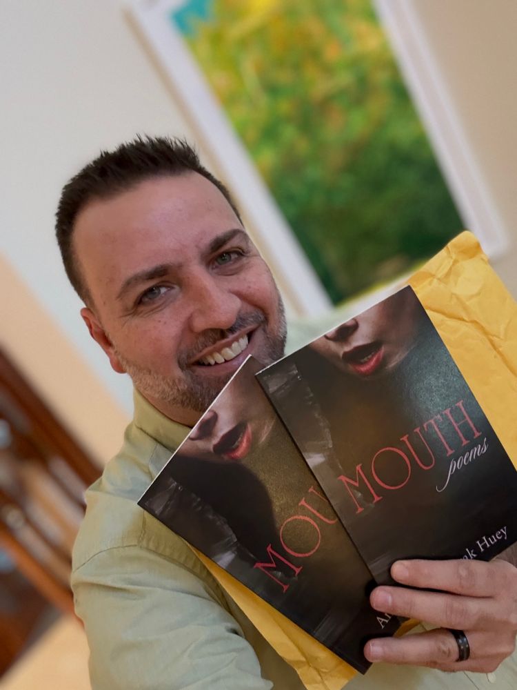 Amorak holding two copies of his poetry book titled Mouth. 