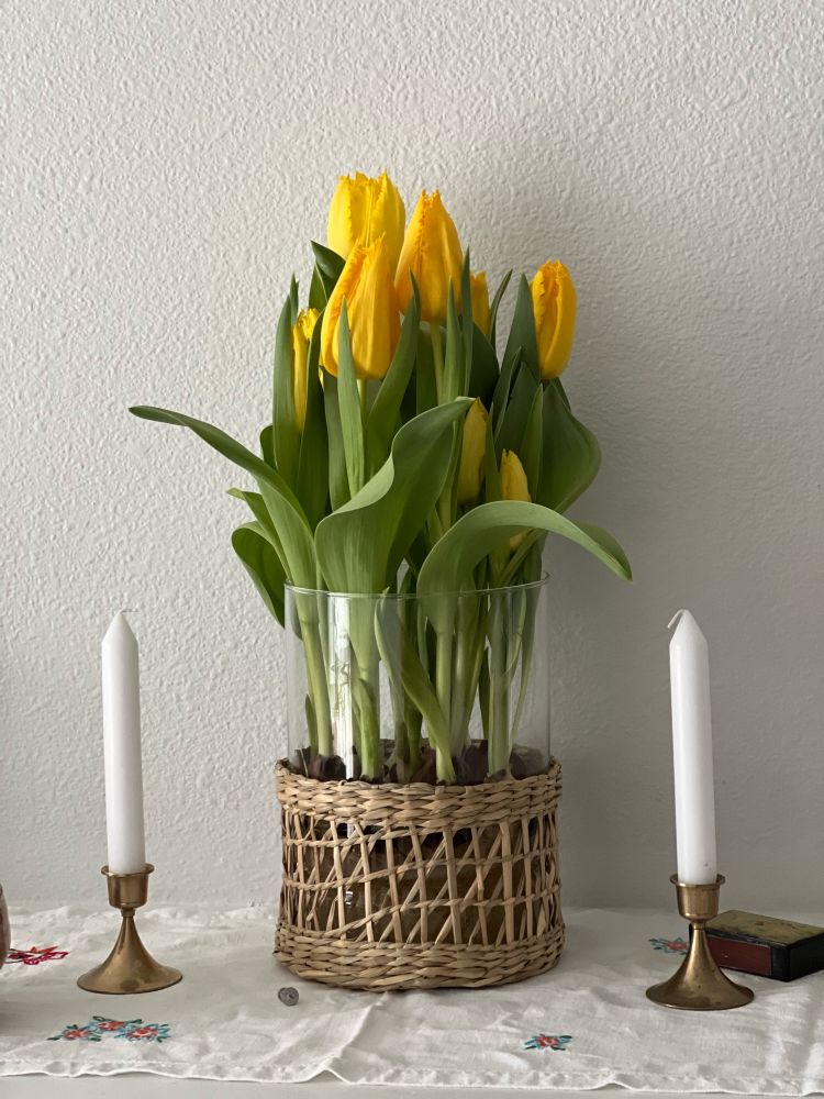 Yellow tulips in a glass vase and a couple of candles 