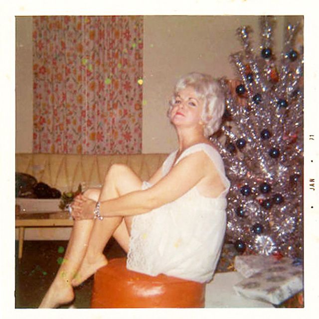 Vintage picture of a woman in a white dress posed next to her silver Christmas tree. 