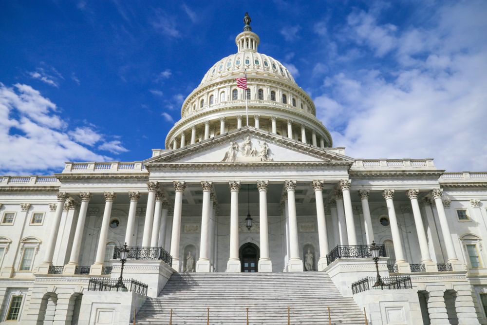 a low-angle photograph of the U.S. Capitol building on a clear-skied day, with light white clouds dotting the blue space behind