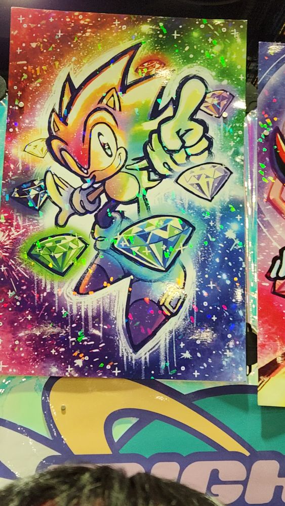 A very sparkly rainbow poster of Sonic the hedgehog with the chaos emeralds