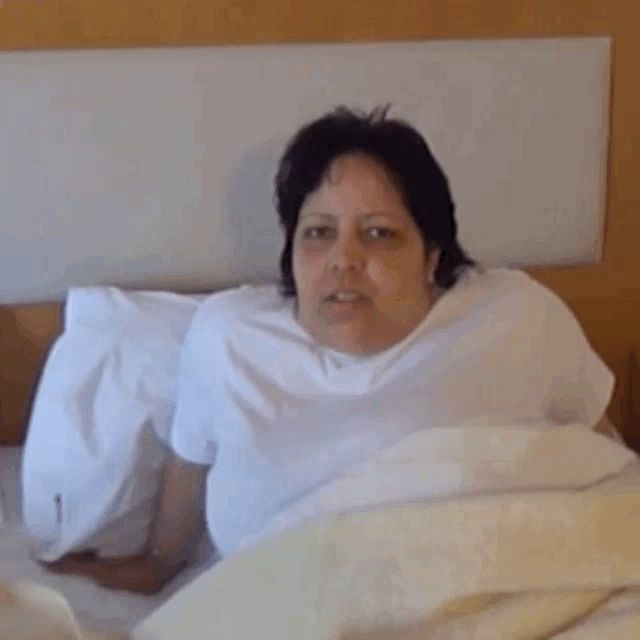 a woman is laying in a bed with a white blanket and a pillow .