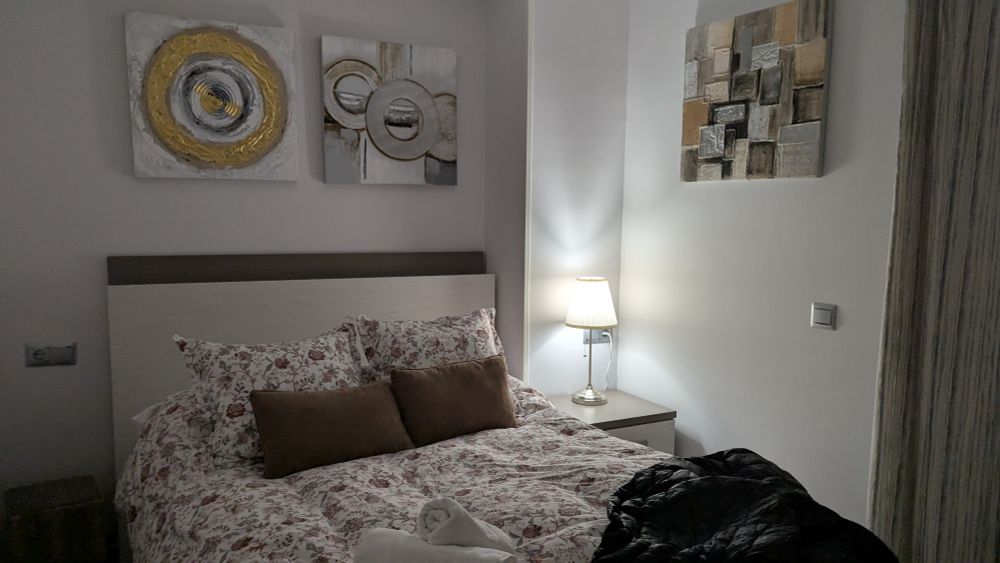 Bedroom with large bed covered with floral duvet. Artwork on walls