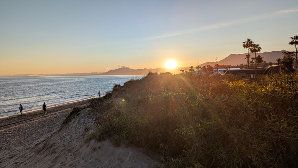 Sunset view over a beach with people walking.