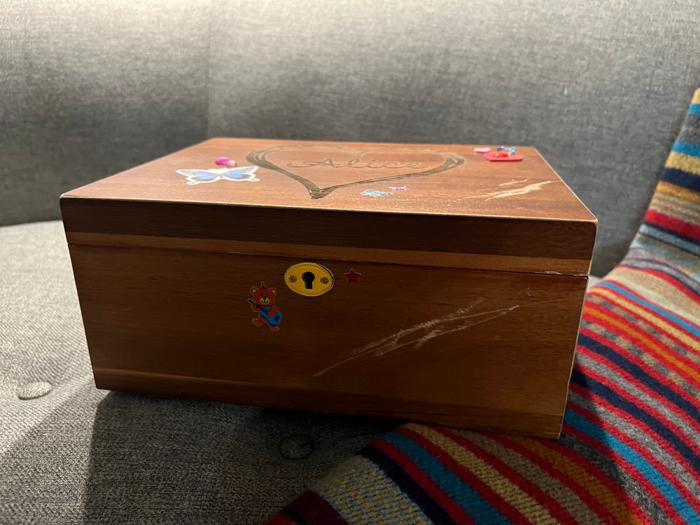 A wooden box photographed from the side, showing a brass lock and additional scrapes and stickers