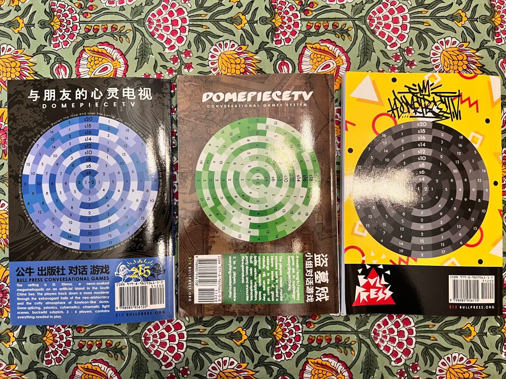 Back covers of three “conversational game” books, each with spirals of numbers to be used as a randomizing tool.
