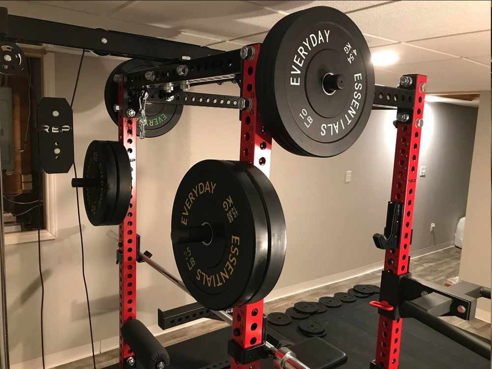 A back view of the same power rack with barbell weights and the lat pulldown pulley system visible.