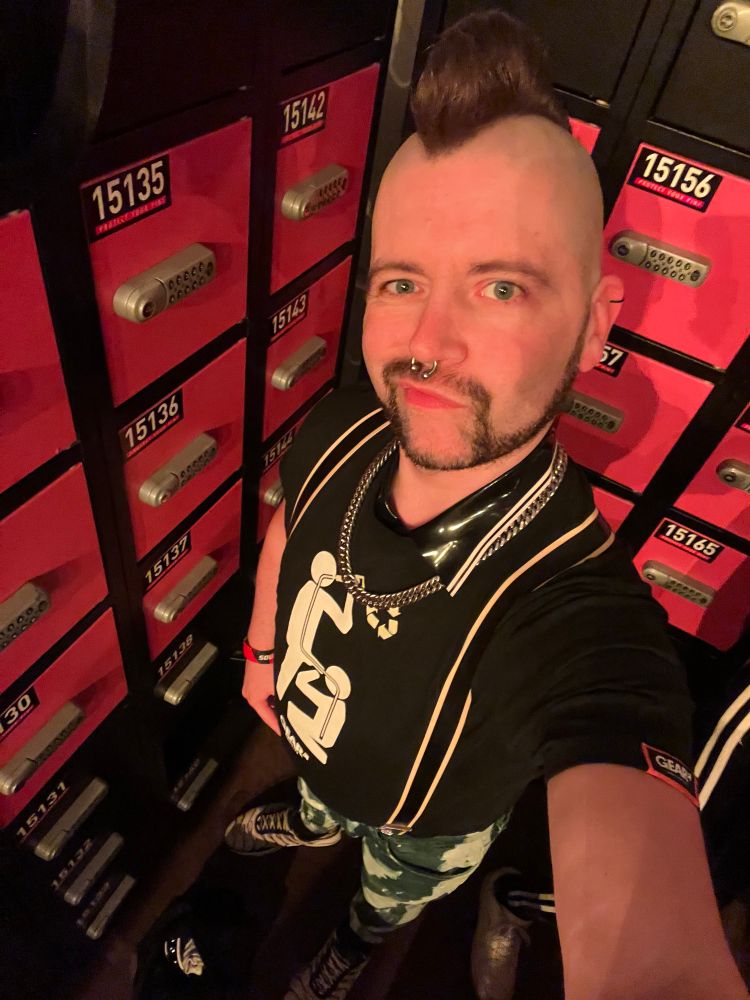 Selfie at the lockers of Darklands. Me wearing yellow sneakers, a bleachers trousers, a shirt with a piss play print and a heavy chain.