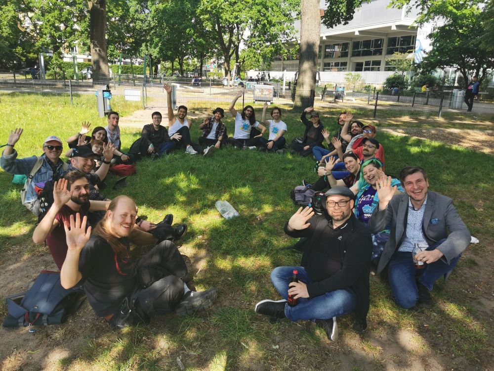 Group sitting in a circle around a bag of pins, waving at the camera
