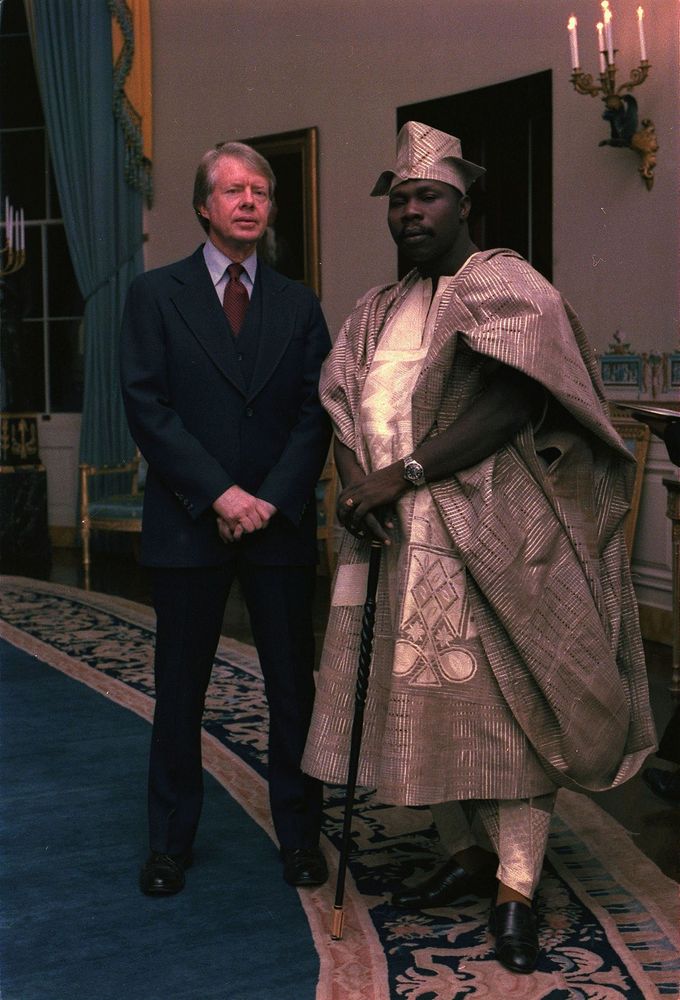 Jimmy Carter and Olusegun Obasanjo standing hands crossed in front of the camera, with mean mug