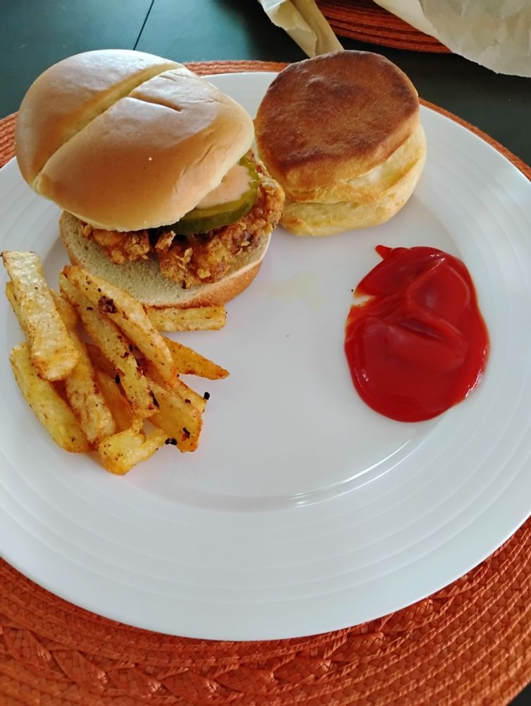 Chicken sandwich, fries, ketchup, and a biscuit on a plate.
