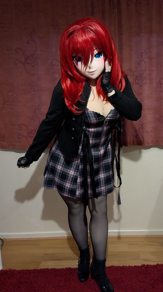 Scarlett, wearing a pink-and-black plaid dress and a black jacket, sheer black tights and black high heels.