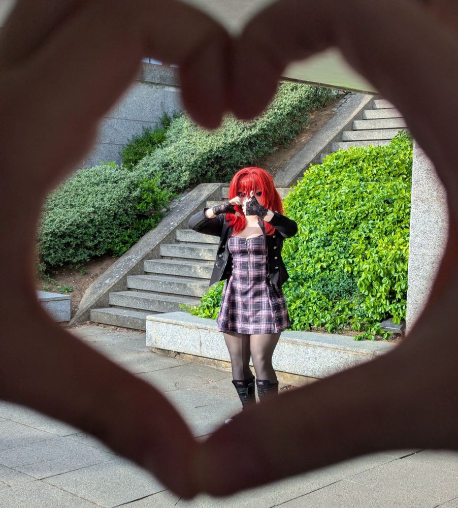 Scarlett standing in an underpass, holding up a 'thumbs up' with one hand and half of a 'heart' with the other. She's framed by a pair of hands doing the correct 'heart' gesture near the camera.