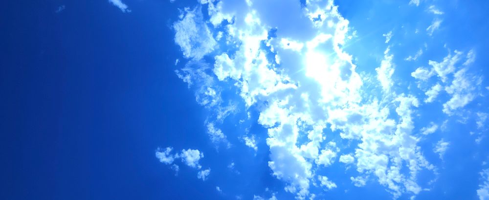 Sunlight forcing itself through a small concentration of clouds towards the right 2/3rds of the picture in a very bright blue sky.