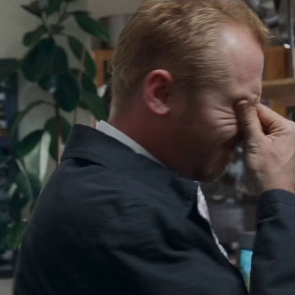 a man is covering his eyes with his hands while wearing a jacket and tie .