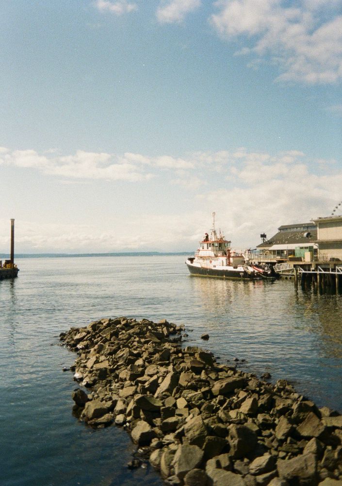 a bunch of rocks leading out to a big bay of water, with a boat docked in frame as well