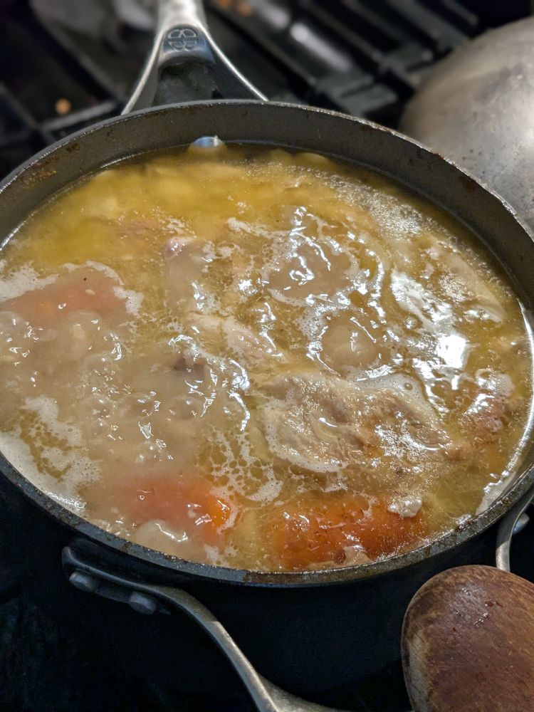 A pot of golden coloured chicken broth simmering on a stovetop.