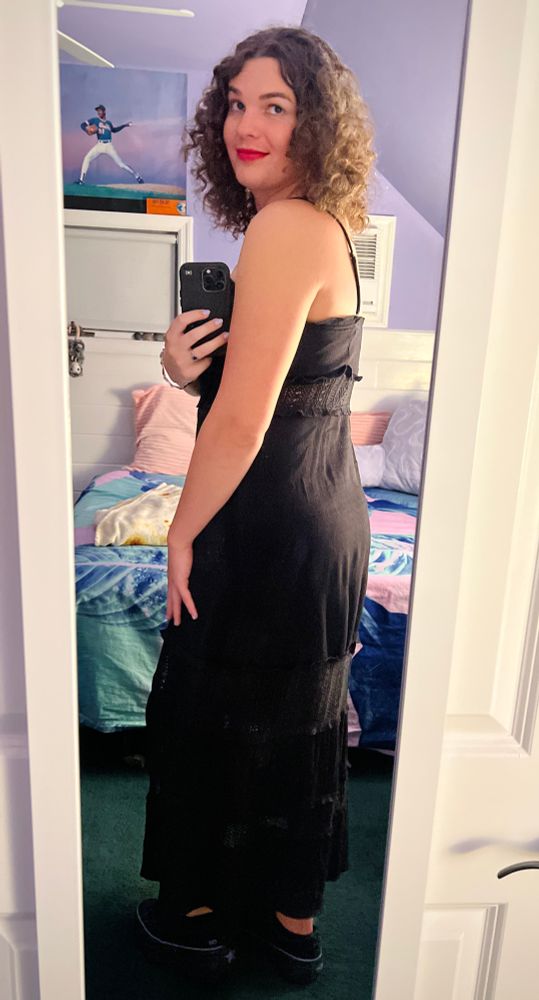 mirror selfie of me wearing a long black spaghetti strap dress, i’m looking over my shoulder seductively and poking my ass out