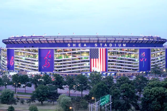 outside of shea stadium during the day with the neon catcher, batter, and pitcher on the exterior walls lit up