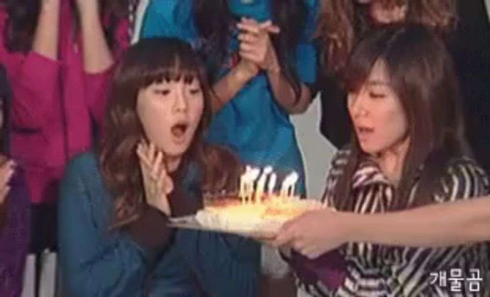 two women are blowing out candles on a birthday cake