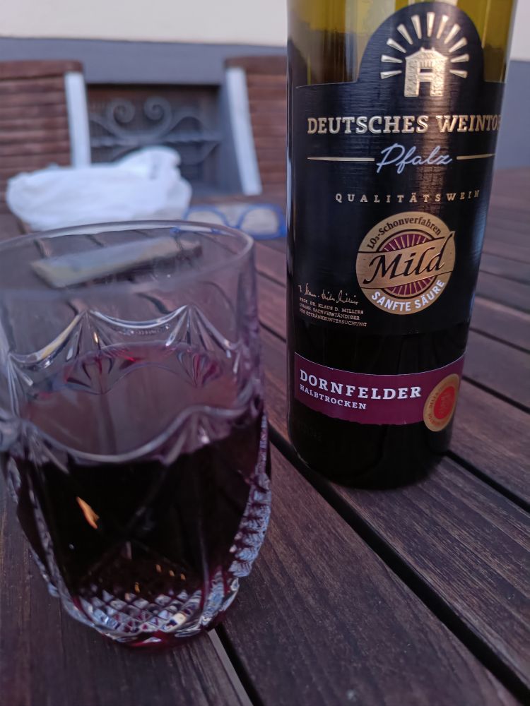 A glass of red wine next to the bottle. Dornfelder halbtrocken.