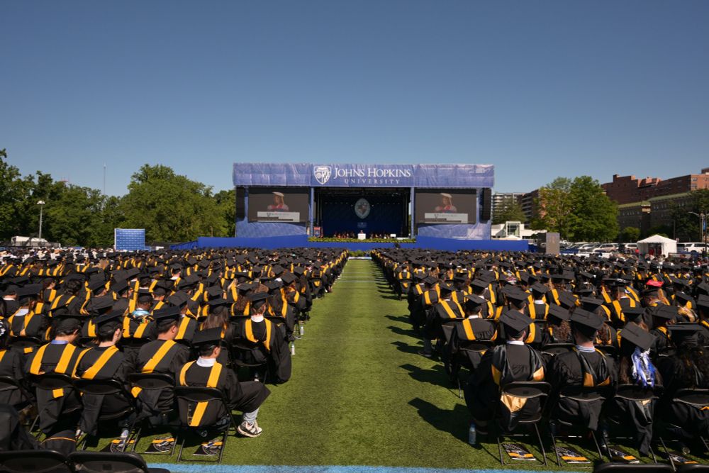 View from behind seated graduates in caps and gowns looking towards the stage. Linda Cureton, Engr '98 (MS), delivers the keynote.