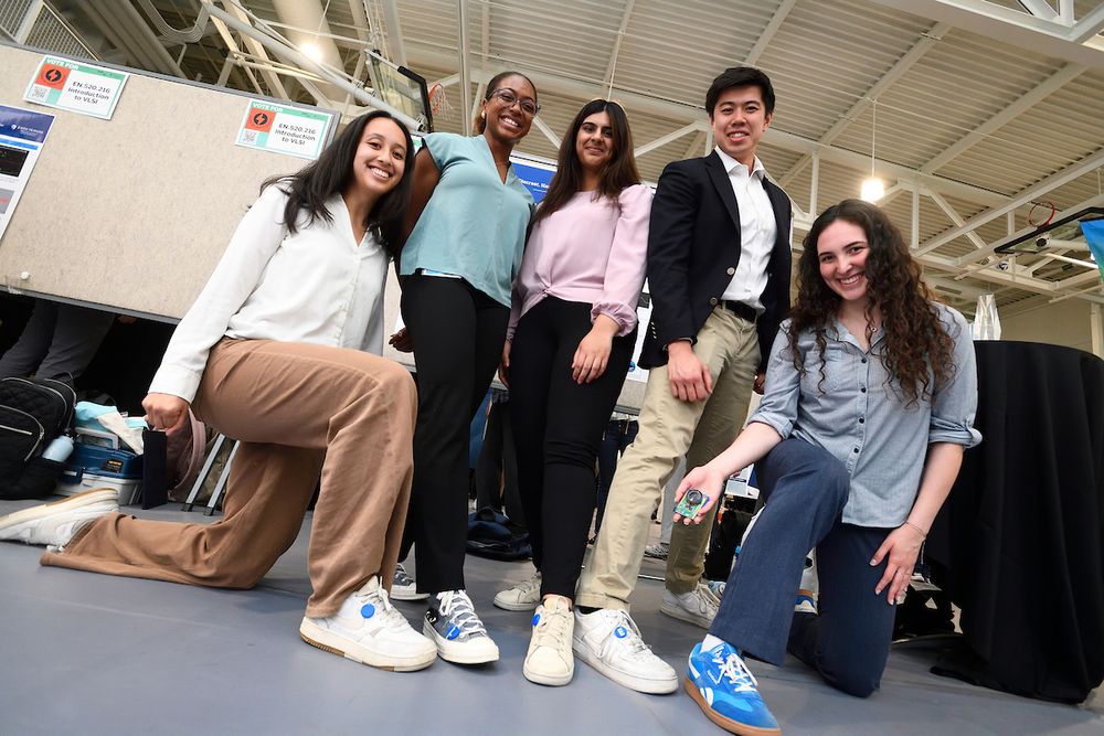 Members of the Chip Charm team in a group photo, stepping forward to show the device on each of their shoes. What team member holds a circuit board. 