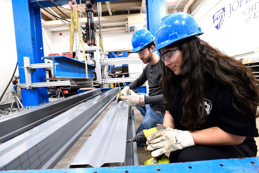 Two students use tools on steel beans in a lab. 